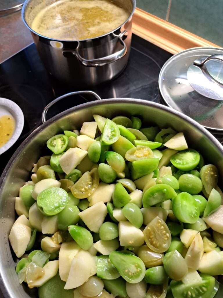 Herd mit einem Topf oben links in dem grüne tomatenkonfitüre köchelt unten rechts sieht man die frischen grünen Tomaten und Apfelstücke in einem Topf, die gleich zu einem Chutney verkocht werden