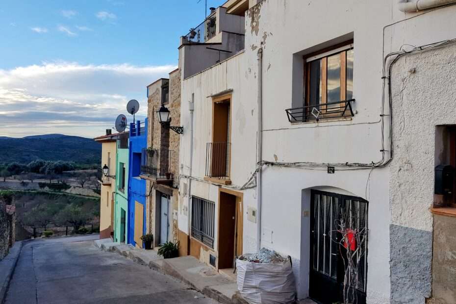 View of a village street. There are little lane houses on the right. The first house with the black door is the one I bought. the street goes on towards the horizon where fields, hills and the sky is visible. The photo is cut off on the left.