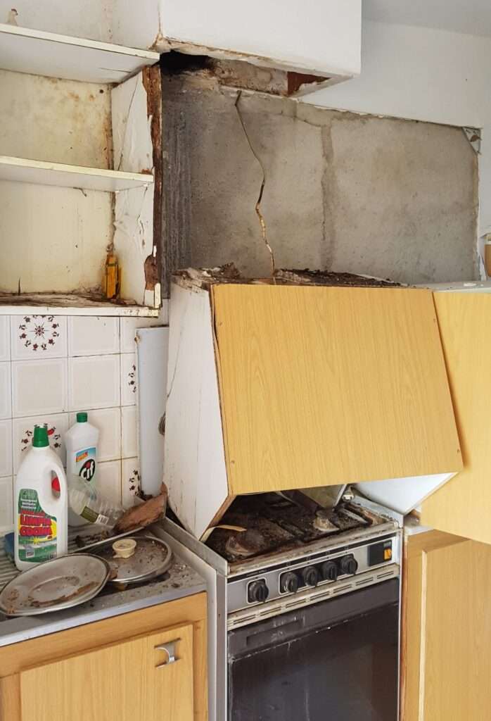 Mouldy chipboard of a fitted kitchen with yellowish veneer, the extractor bonnet has fallen onto the soiled stove.
